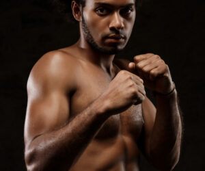 Young sportive african man posing over black background.